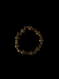 A beaded stretch bracelet made of polished brown and gold-toned gemstone beads, displayed on a plain off-white surface.